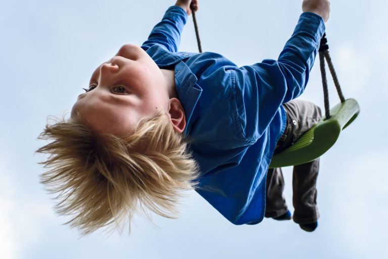 Kind speelt ondersteboven met een blije uitdrukking tegen een blauwe hemel.