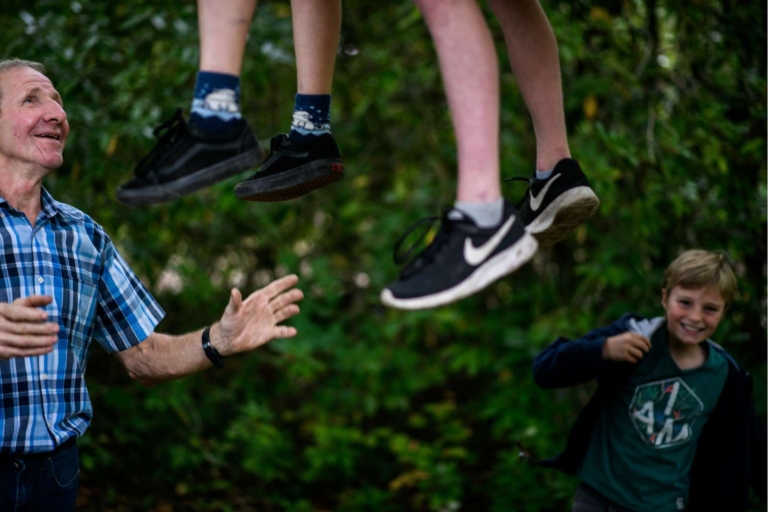 Man in geruite blouse kijkt naar blije kinderen die buiten spelen.