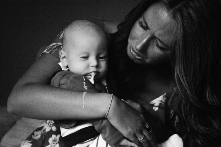 Vrouw wiegt baby, beiden ontspannen, in knusse sfeer.