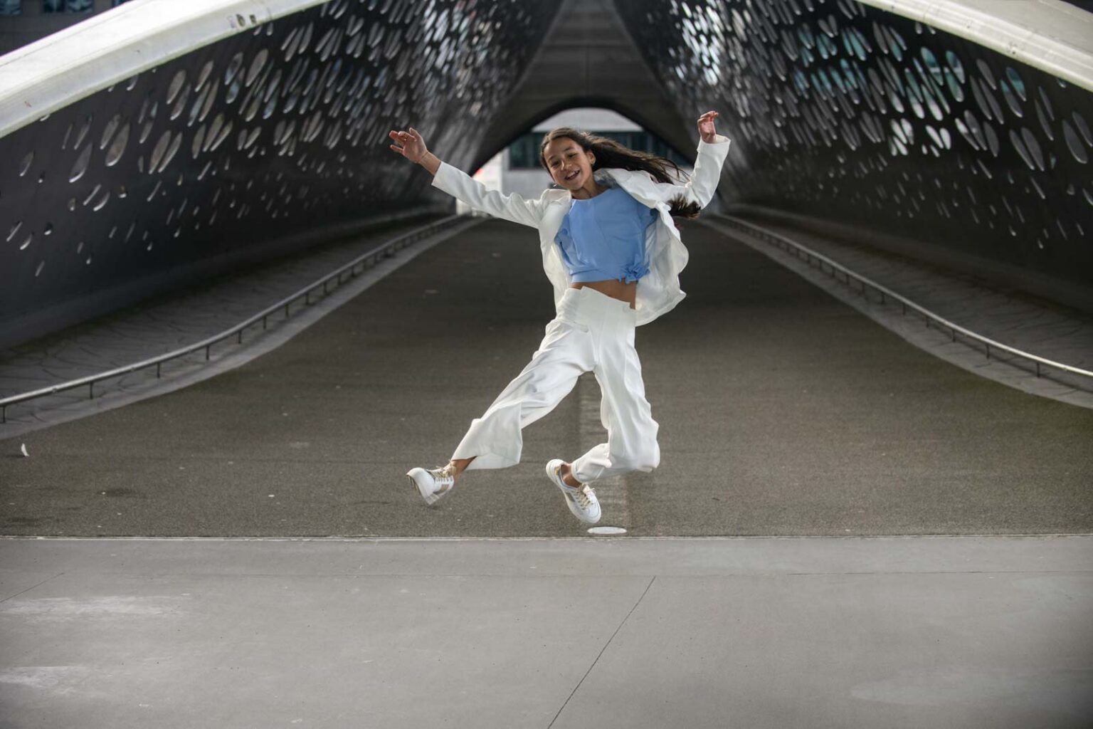 Vrolijke vrouw in wit pak springt op een moderne, tunnelachtige brug.